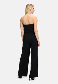Zwarte strapless jumpsuit met brede pijpen, een rits aan de achterkant en een getailleerd lijfje. Glad stof met een lichte glans.