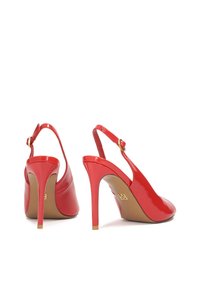 Punaiset lakatut nahka-slingback-kengät, joissa on korkeat stiletto-korkot, säädettävä nilkkaremmim ja sileä viimeistely takana.
