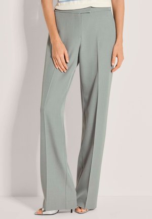 Hellgraue, weit geschnittene Hose aus glattem Stoff, mit flachem Vorderteil und dezenten Falten, kombiniert mit Riemchen-Sandaletten mit Absatz.