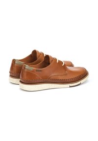 Scarpe in pelle marrone con finitura liscia, dotate di una suola chiazza chiara, design con lacci e cuciture decorative lungo i bordi.
