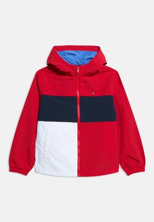 Veste rouge à capuche avec une bande horizontale marine et un panneau inférieur blanc, fermeture éclair à l'avant, poignets élastiques et poches latérales, doublure intérieure bleue visible.