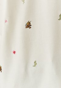 Wit stoffen met kleurrijke geborduurde ontwerpen: een gele bij, een roze bloem en groene bladeren, wat zorgt voor een speelse patroon.