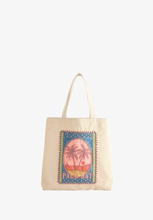 Beige draagtas met stoffen patch waarop twee palmbomen, oceaan, zonsondergang, vogels en de tekst "PALM BAY" in roze en blauwe kleuren zijn afgebeeld.