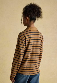 Pikad varrukad pruunist ja tumesinisest triibulisest särgist, millel on krae ja vabam lõige. Valmistatud pehmest kangast, millel on tekstureeritud viimistlus.