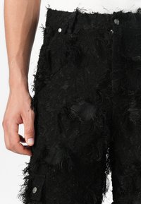 Schwarze, ausgefranste Cargo-Hosen aus strukturiertem Stoff. Mit Seitentaschen, Knopfverschluss und unregelmäßigen Saumdetails.
