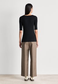 Zwart getailleerd topje met korte mouwen, gecombineerd met hooggewaisted beige broek met ruime pijpen. Het schoeisel heeft een stevige hak en een uniek patroon.