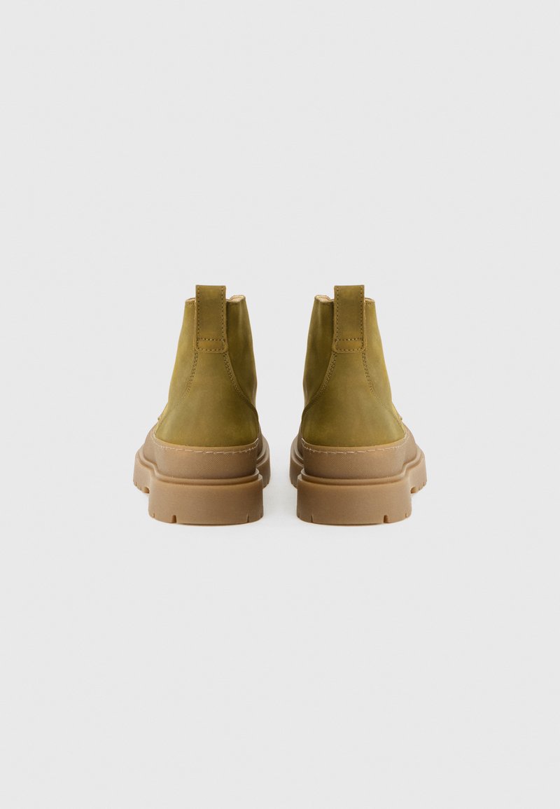 Botas de tobillo de ante verde con un acabado texturizado, que cuentan con una suela de goma marrón gruesa y lengüetas en la parte trasera para ponerlas y quitarlas con facilidad.