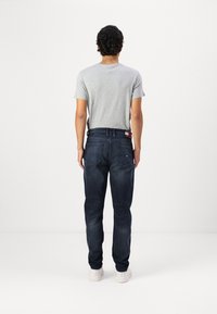 Mørkeblå denimjeans med rette ben, kombinert med en grå t-skjorte med korte ermer. Merkedetaljer inkluderer baklommer og en merkevarebelte.