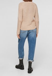 Pull en tricot beige avec une finition texturée, associé à un jean bleu ample. Des bottines noires à semelle épaisse sont également visibles.