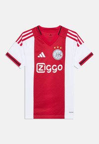 Maglia da calcio rossa e bianca con design a collo a V, tre strisce rosse sulle spalle, logo del club e testo dello sponsor in caratteri in grassetto.