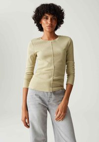 Hellgrünes, geripptes Langarmoberteil mit rundem Ausschnitt und Vordernahtdetail, kombiniert mit hellgrauen, weiten Jeans.