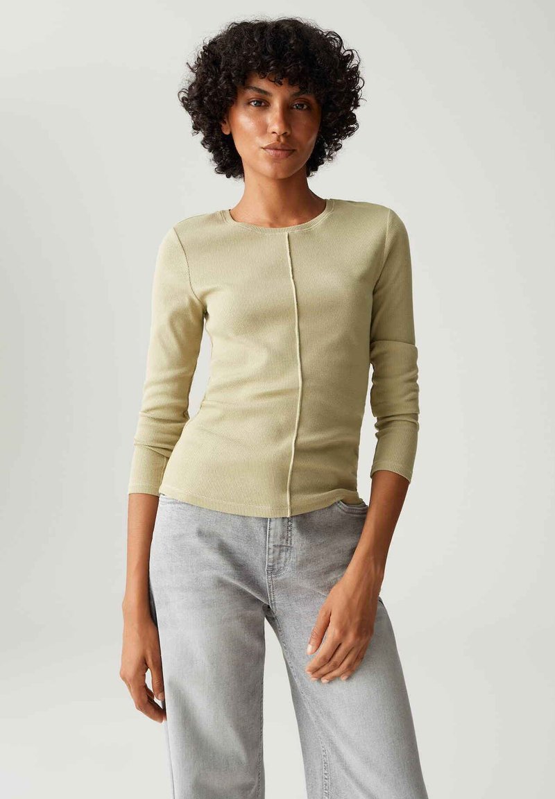 Hellgrünes, geripptes Langarmoberteil mit rundem Ausschnitt und Vordernahtdetail, kombiniert mit hellgrauen, weiten Jeans.