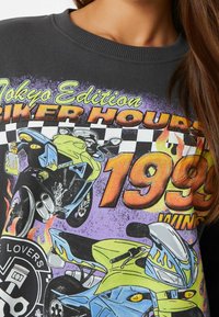 Sudadera gris con un diseño gráfico colorido que presenta motocicletas, llamas y texto. El texto dice "Edición Tokio Horas de Motocicleta 1999 Ganadas."
