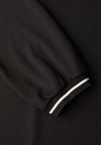 Musta collegepaita, jossa on teksturoitu pinta. Hihansuun resorissa on musta-valkoinen raidallinen neulekuvio, joka tarjoaa värikontrastin.