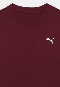 Camiseta burdeos de algodón suave, con cuello redondo y un logo de Puma bordado en blanco en el lado izquierdo del pecho. Diseño sencillo.