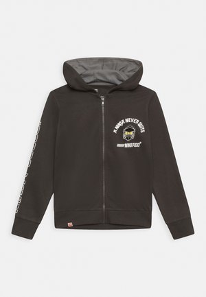 Sort zip-up hoodie med grå indvendig, teksten "A Ninja Never Quits" og et Ninjago-graphic på brystet; lange ærmer med tekstdetalje.