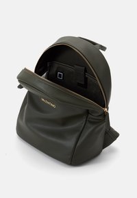 Green textured leather backpack with a zip closure, gold hardware, and a spacious interior featuring a pocket and adjustable straps.