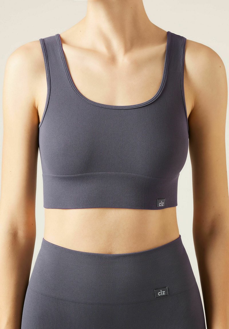 Grå ribbet crop top med en scoop halsudskæring og brede stropper. Har et mærketiket i kanten. Glat tekstur og tætsiddende design.