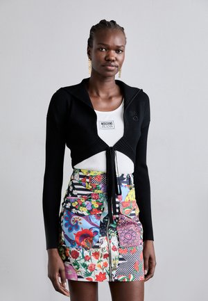 Svart ribbestrikket cropped cardigan med sjalkrage og frontknyting, kombinert med et flerfarget blomster- og mønstrete miniskjørt.