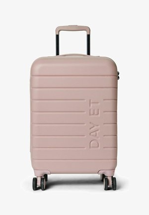 Valise rigide de couleur rose clair, avec une surface texturée, des bords arrondis, des rainures verticales et une poignée télescopique. Quatre roues multidirectionnelles.