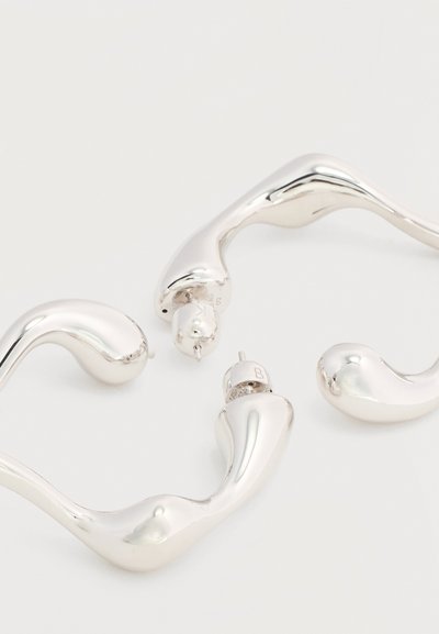 Ζευγάρι ακανόνιστου σχήματος, λαμπερά ασημένια σκουλαρίκια κρίκοι με κλείσιμο πίσω με καρφί, σε λευκό φόντο.