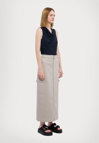 Mørkeblå ærmeløs top med draperet halsudskæring, parret med en lysegrå, knælang nederdel med lynlås foran og sidelommer. Sorte platform sandaler.