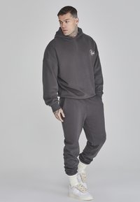 Felpa con cappuccio grigio carbone e pantaloni sportivi abbinati con una vestibilità comoda. Polsini rinforzati e dettaglio logo sul petto. Sneakers bianche.