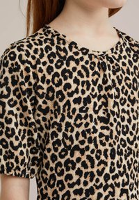 Majica s leopard uzorkom koja sadrži crno-bež shemu boja, kratke rukave i okrugli izrez, izrađena od teksturirane tkanine.