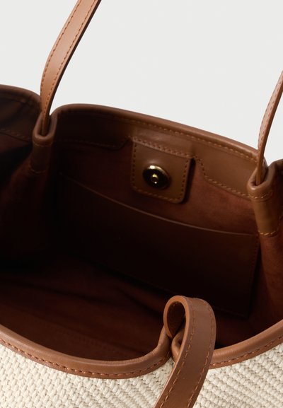 Καφέ υφασμάτινη τσάντα με δερμάτινη επένδυση, δύο λαβές, ανοιχτό επάνω μέρος και εσωτερική θήκη ασφαλισμένη με χρυσό κουμπί πάτημα.