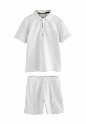 Camisa polo blanca con cremallera de un cuarto y un pequeño logo, combinada con pantalones cortos blancos a juego con cierre de botón y pliegues.