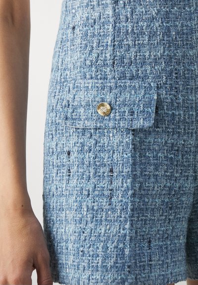 Pantaloni scurți din tweed texturat, de culoare albastru deschis, având un mic buzunar cu clapetă și închidere cu buton aurit. Țesătura are un model stropit.