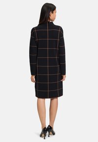 Svart stickad klänning med orange rutmönster, långa ärmar, hög halsringning och knälång längd, lämpad med glansiga svarta klackar.
