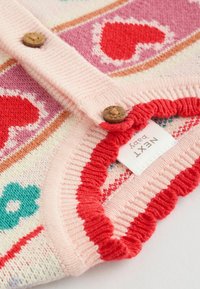 Strickjacke in Rosa mit Herzmustern in Rot und Rosa, ausgestattet mit Holzknöpfen und einem Rüschensaum. Inklusive eines Bekleidungslabels.