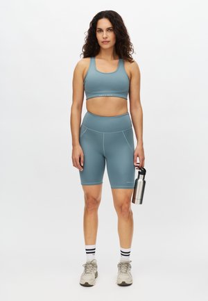 Light blue sports bra and bike shorts made of smooth fabric. Features fitted design, white stitching, and a silver water bottle.