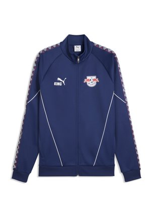 Veste de sport bleu marine à fermeture éclair avec le logo RB Leipzig, le logo Puma, le texte "KING" et des rayures à motifs le long des manches.