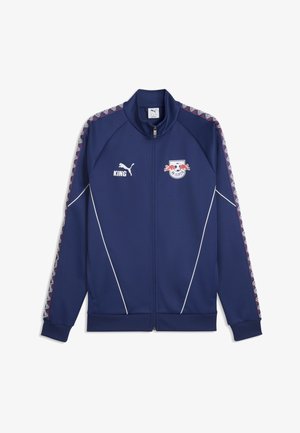 Veste de sport bleu marine à fermeture éclair avec le logo RB Leipzig, le logo Puma, le texte "KING" et des rayures à motifs le long des manches.
