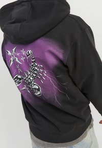 Felpa nera con una sfumatura viola e nera. Presenta una grande grafica di uno scorpione e stelle sulla schiena. Tessuto morbido e texturizzato.