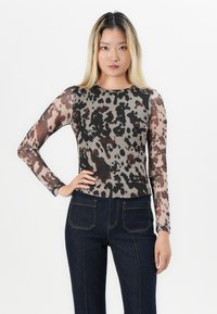 Haut à manches longues en tissu transparent avec un imprimé animal abstrait beige et noir. Associe à un jean taille haute bleu foncé.