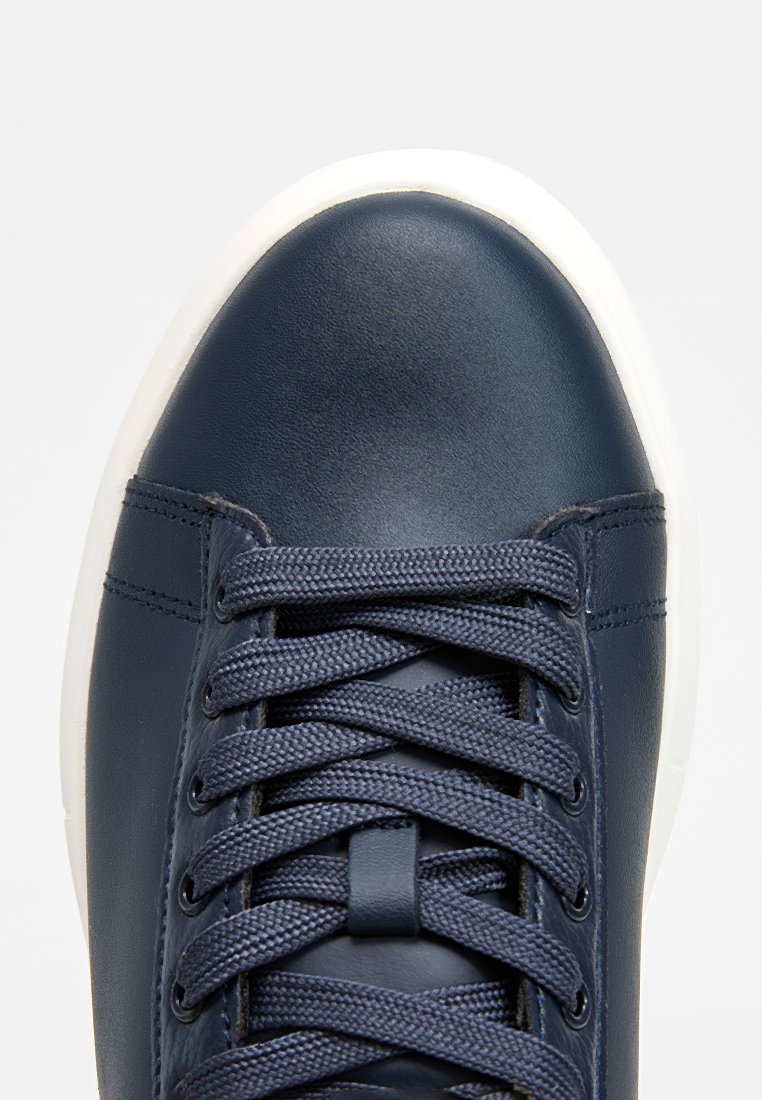 Baskets en cuir bleu marine avec semelle en caoutchouc blanc, dotées de six œillets, de lacets plats bleu marine et d'une texture lisse sur le bout.