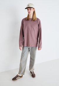 Langermet mauve skjorte i myk bomull, sammen med lyse denimjeans. Antrekket fullføres med brune sneakers og en beige caps.