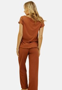 Ensemble deux pièces côtelé de couleur rouille comprenant un haut ample à manches courtes et un pantalon à jambes larges, avec une finition texturée et une coupe décontractée.