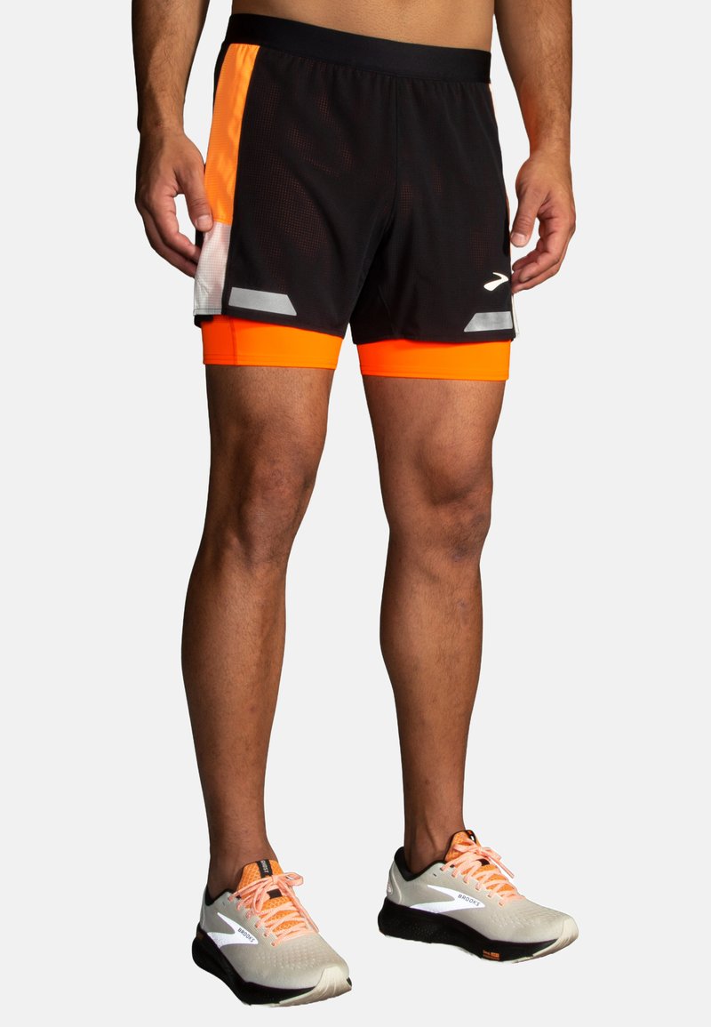 Svarta springshorts med orange och grå detaljer, med ett mesh-material och en slim fit. Kombineras med ljusgråa sneakers.