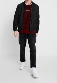 Sort bomberjakke med netærmer, marnov sweatshirt med hvide detaljer, mørke jeans og hvide sneakers.