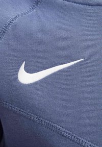 Tissu de sportswear bleu avec une texture lisse présentant un logo Nike swoosh blanc bien en vue, complété par des détails de couture contrastants.