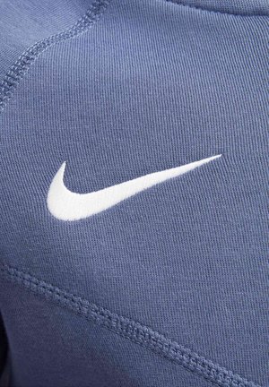 Blå sportklädesmaterial med en slät textur har en framträdande vit Nike-swoosh-logotyp, kompletterad med kontrasterande sömdetaljer.