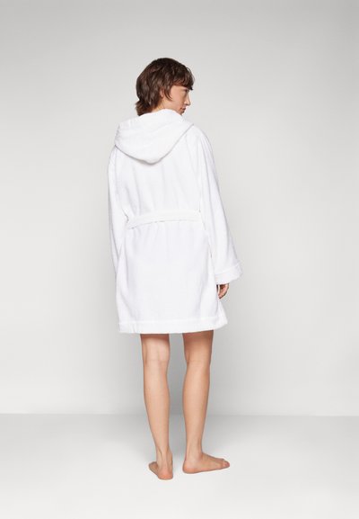 White terry cloth bathrobe with a hood, belted waist, long sleeves, and a soft, textured finish. Worn barefoot, showcasing a casual design.