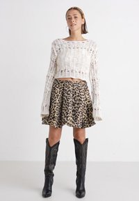 Suéter corto de punto blanco, falda de campana con estampado de leopardo, botas negras de cuero hasta la rodilla con costuras decorativas.