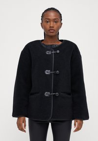 Čierny fleecový kabát s okrúhlym výstrihom, uzávermi na pracku a bočnými vreckami. Dizajn obsahuje textúrovanú látku a voľný strih.