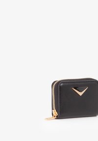 Portafoglio in pelle nera con zip dorata. Presenta un accento logo triangolare sulla parte anteriore. Forma quadrata, texture liscia, design compatto.