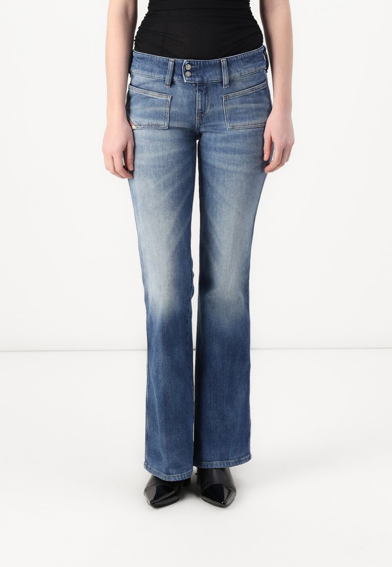 Jeans a zampa d'elefante in denim blu con una lavatura sbiadita, tasche frontali e chiusura a doppio bottone. Abbinati a scarpe nere con tacco.